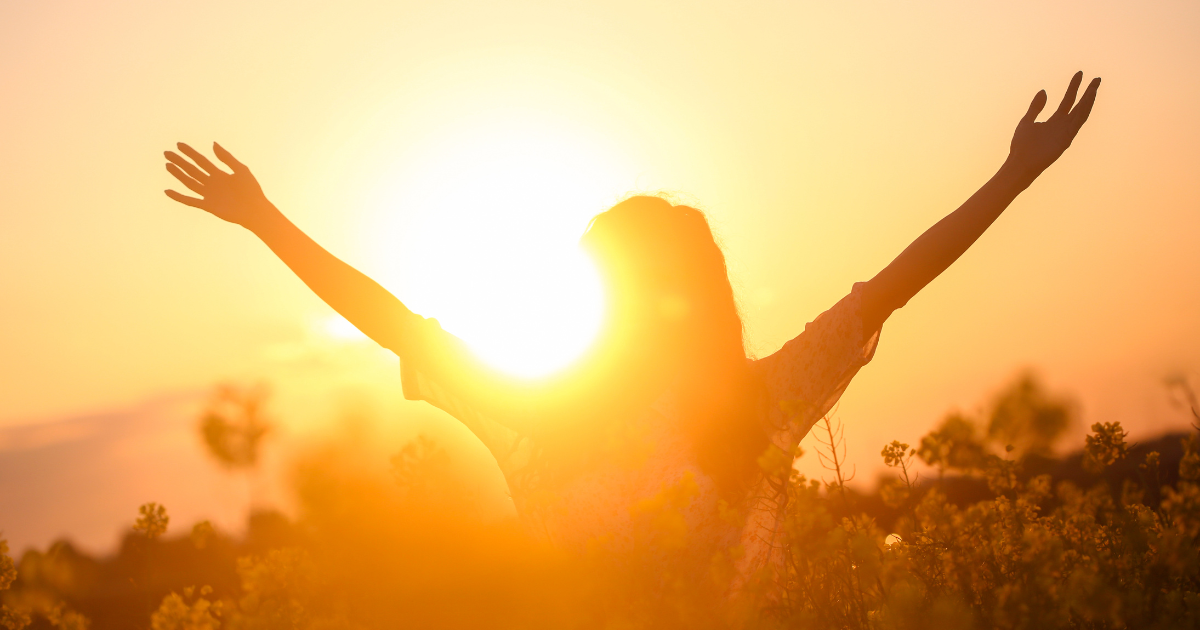 A woman facing the sun with her hands above her head #HappinessQuotes #BlissfulMoments
