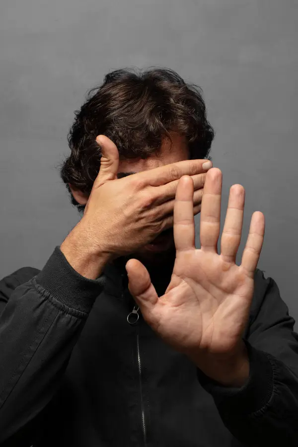 A man hiding his eyes, gesturing "no"